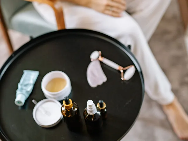 Skincare jars, a dropper bottle and a jade roller arranged on a dark round tray, shot from above.