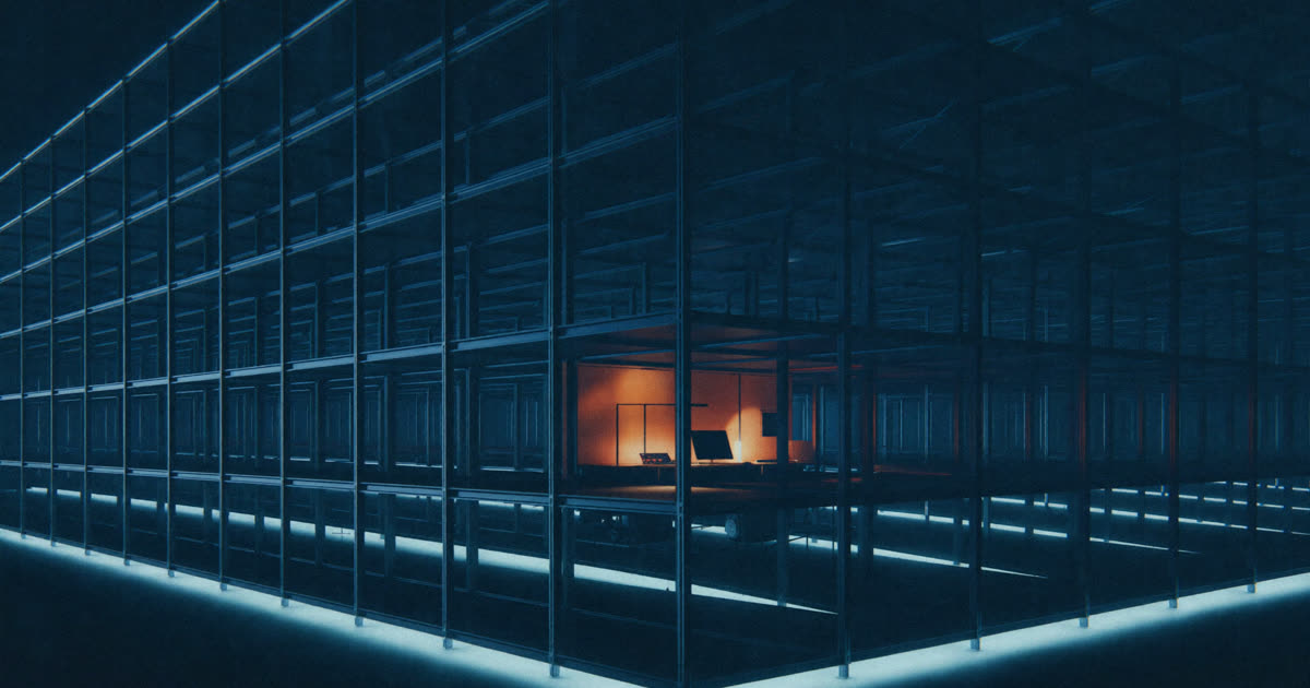 A vast dark grid of warehouse racking with one small warmly lit workstation, illustrating the scale contrast behind warehouse staff turnover.