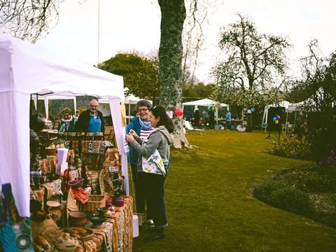 A white marquee stall at an outdoor fair with visitors browsing the table.