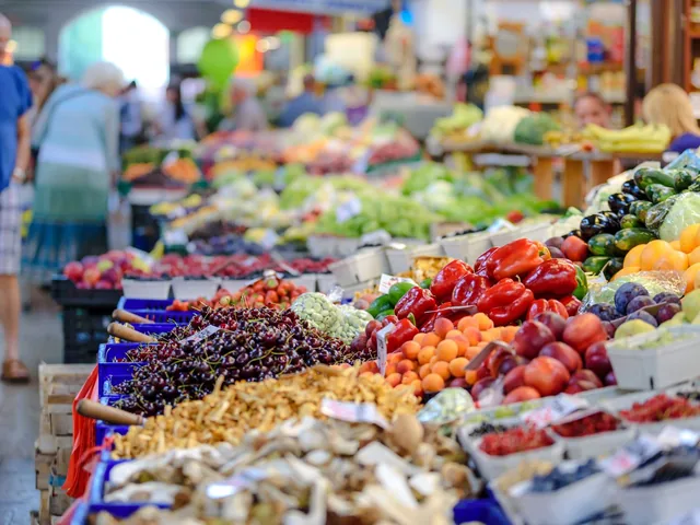 An open market stall stacked with produce, with shoppers standing along it.