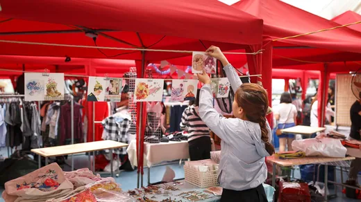 A shopper reaching across a red canopy market stall to take something from the display.