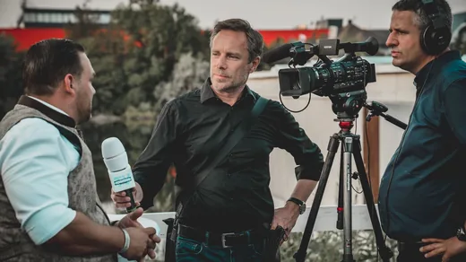 A camera on a tripod and a handheld microphone set up to record someone outdoors.