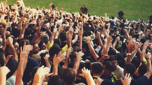 A dense crowd at an outdoor event with hundreds of hands in the air.